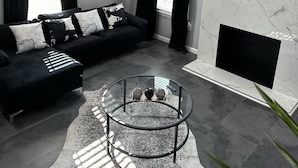 Un saló modern amb un sofà negre, una taula de centre de vidre i una llar de foc.