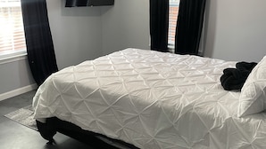 Un dormitori amb un llit, un televisor fixat a la paret, un ventilador de sostre i una taula rodona petita.