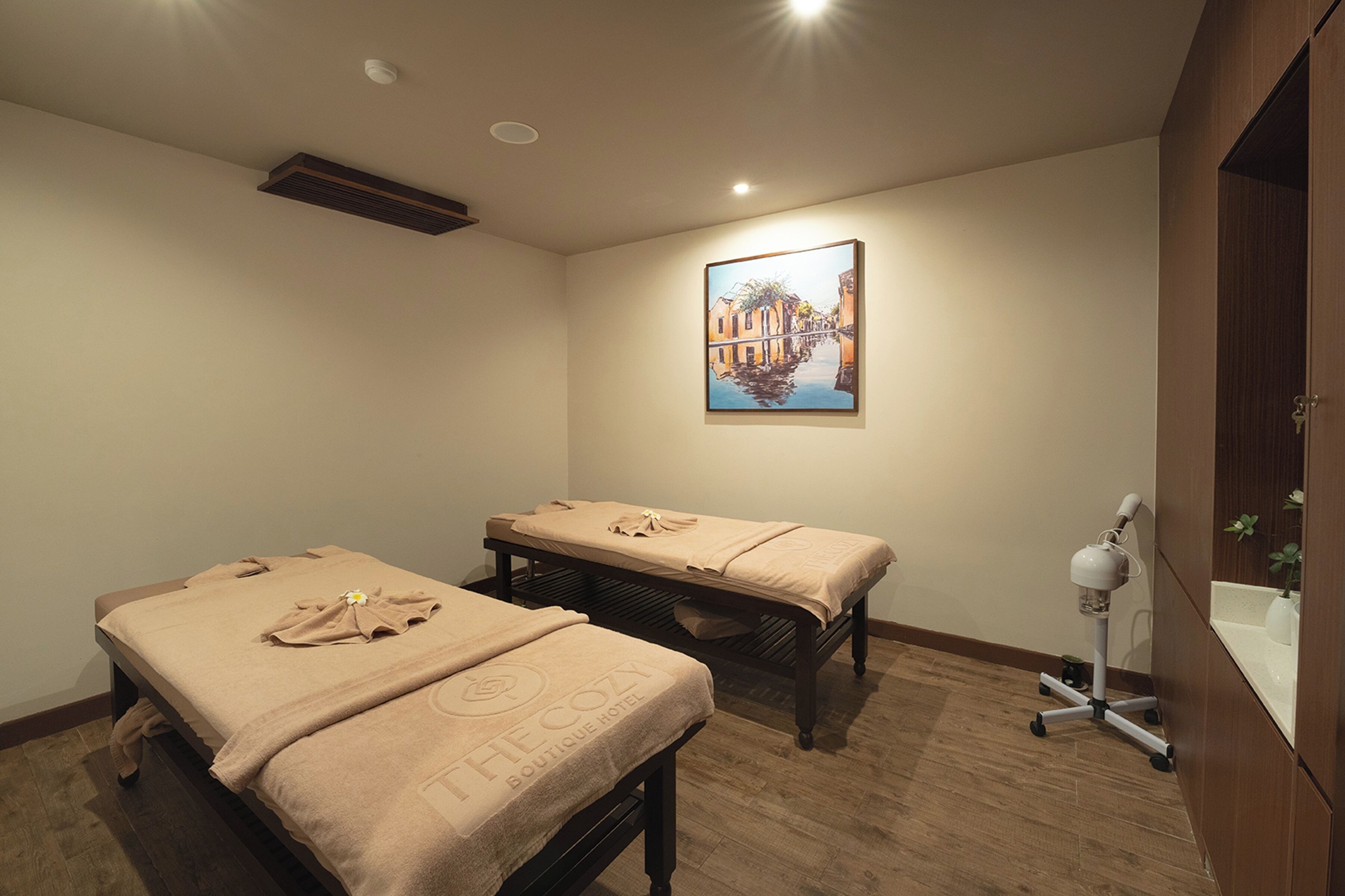 Une pièce comprenant deux tables de massage, un tableau au mur et un petit bureau avec une lampe.