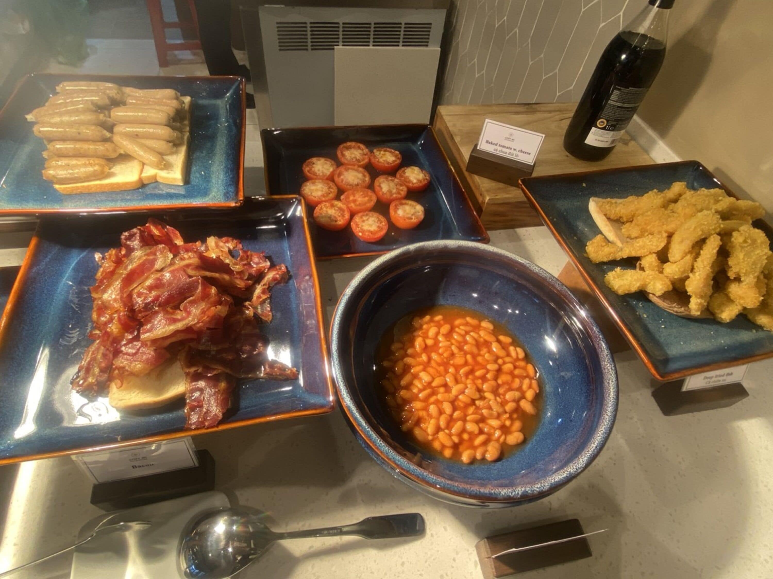 A buffet with various dishes including bacon, baked tomatoes, beans, and fried items.