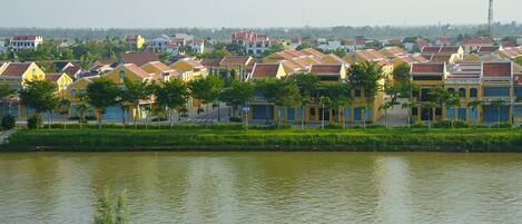 A row of yellow buildings with red roofs along a riverbank.