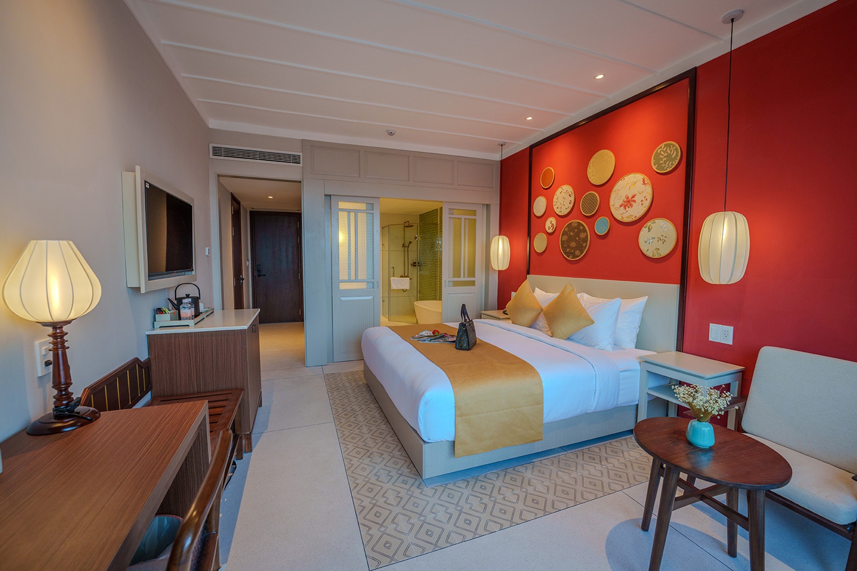 A hotel room with a bed, bedside table, lamp, and a wall decorated with plates.