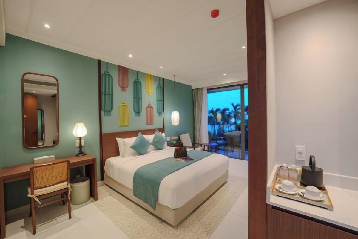A hotel room with a bed, desk, chair, and a view of palm trees.
