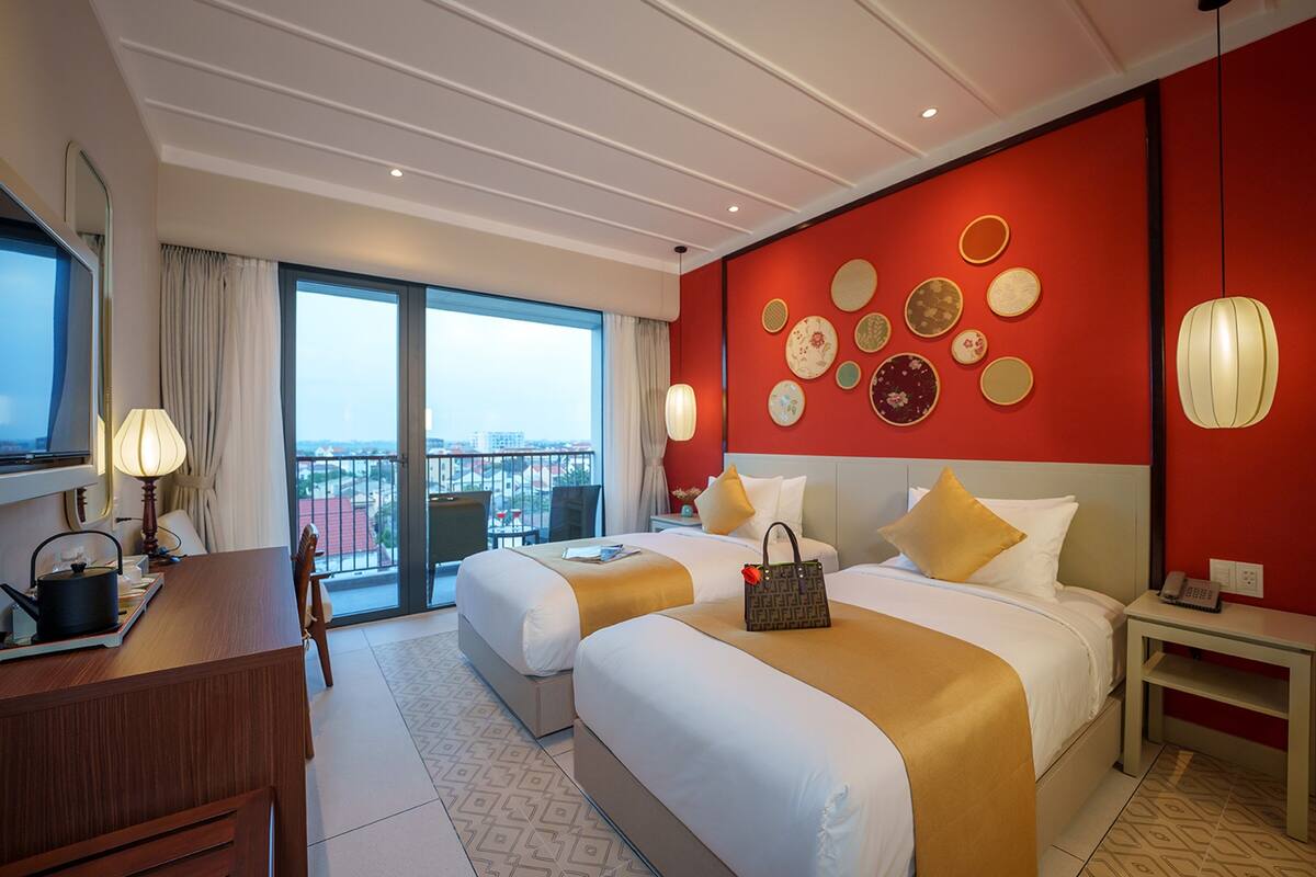 A hotel room with two beds, a desk, and a view of the city.