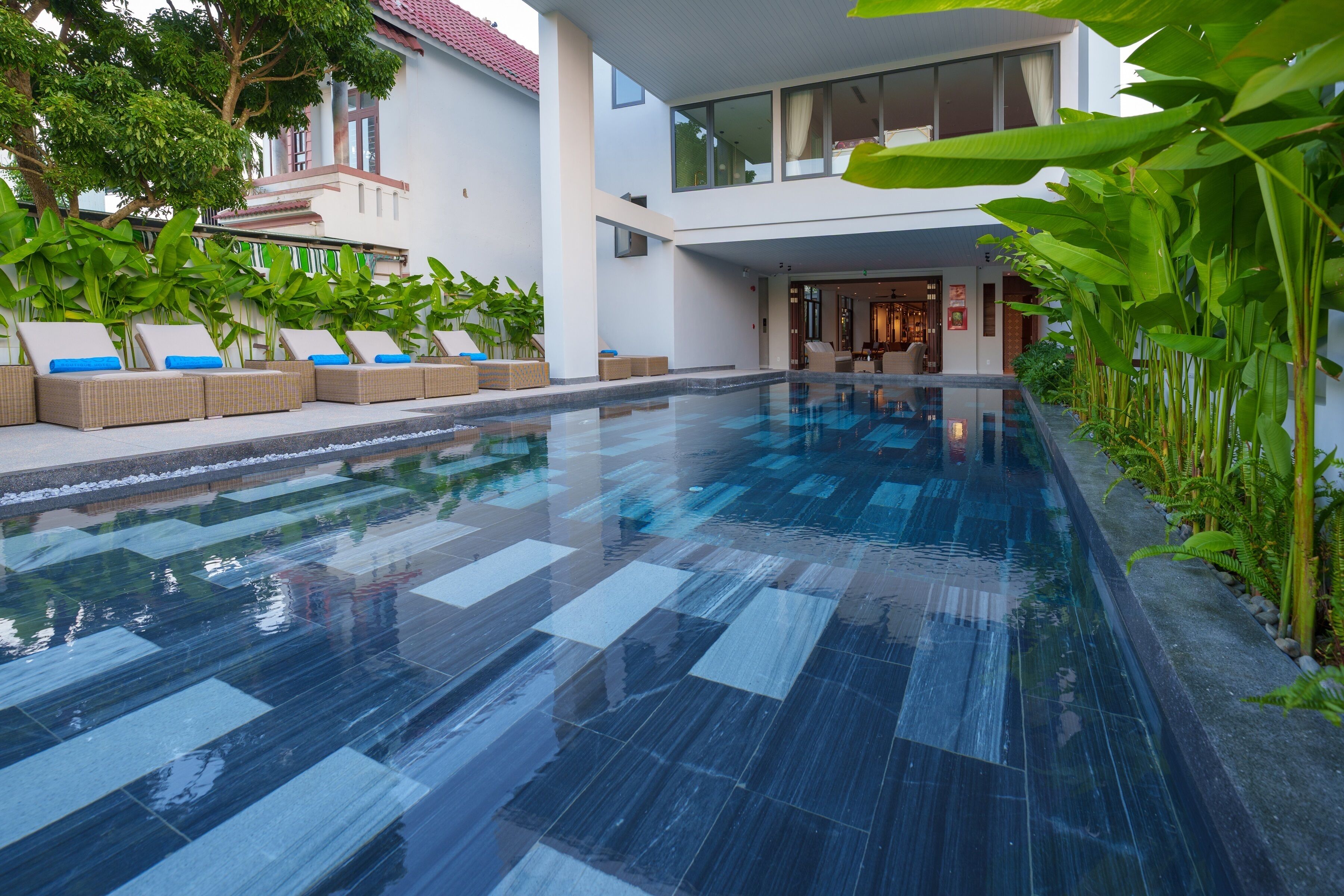 A modern hotel with a swimming pool, outdoor seating, and lush greenery.