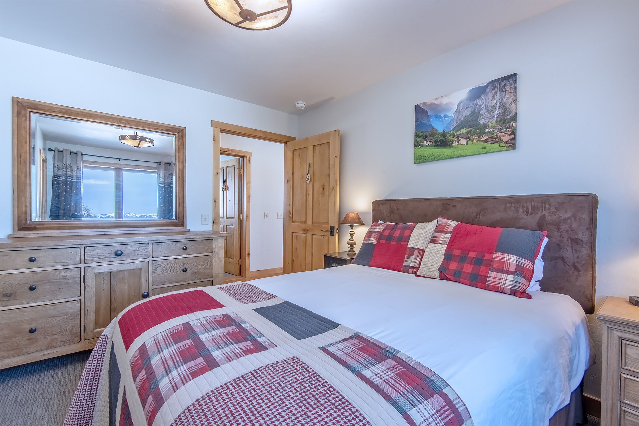 A bedroom with a large bed, wooden dresser, and a painting on the wall.