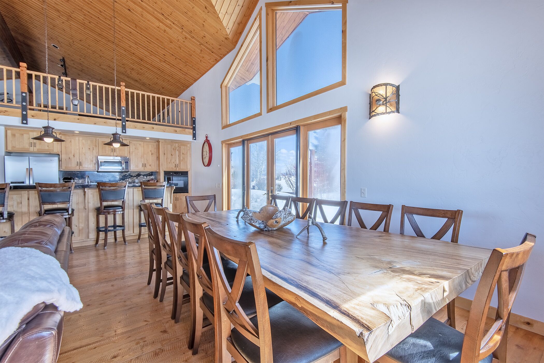 A spacious dining area with a large wooden table and chairs, a kitchen with wooden cabinets and a lofted seating area.