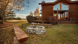 A wooden cabin with a stone fire pit, a wooden deck, and a large window overlooking the landscape. - Spacious 5BR Mountain Retreat near Grand Targhee (Driggs)