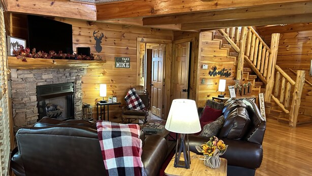 A cozy cabin interior with a stone fireplace, wooden walls, a leather sofa, and a staircase. - Alpine Adventure - Mountian home close to attractions! (Pigeon Forge)