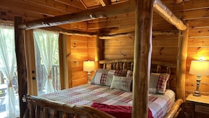 A wooden four-poster bed with a quilt and pillows, a nightstand with a lamp, and a window with curtains. - Alpine Adventure - Mountian home close to attractions! (Pigeon Forge)