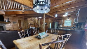 A wooden interior with a dining table, chairs, a chandelier, a staircase, and a kitchen area. - Alpine Adventure - Mountian home close to attractions! (Pigeon Forge)