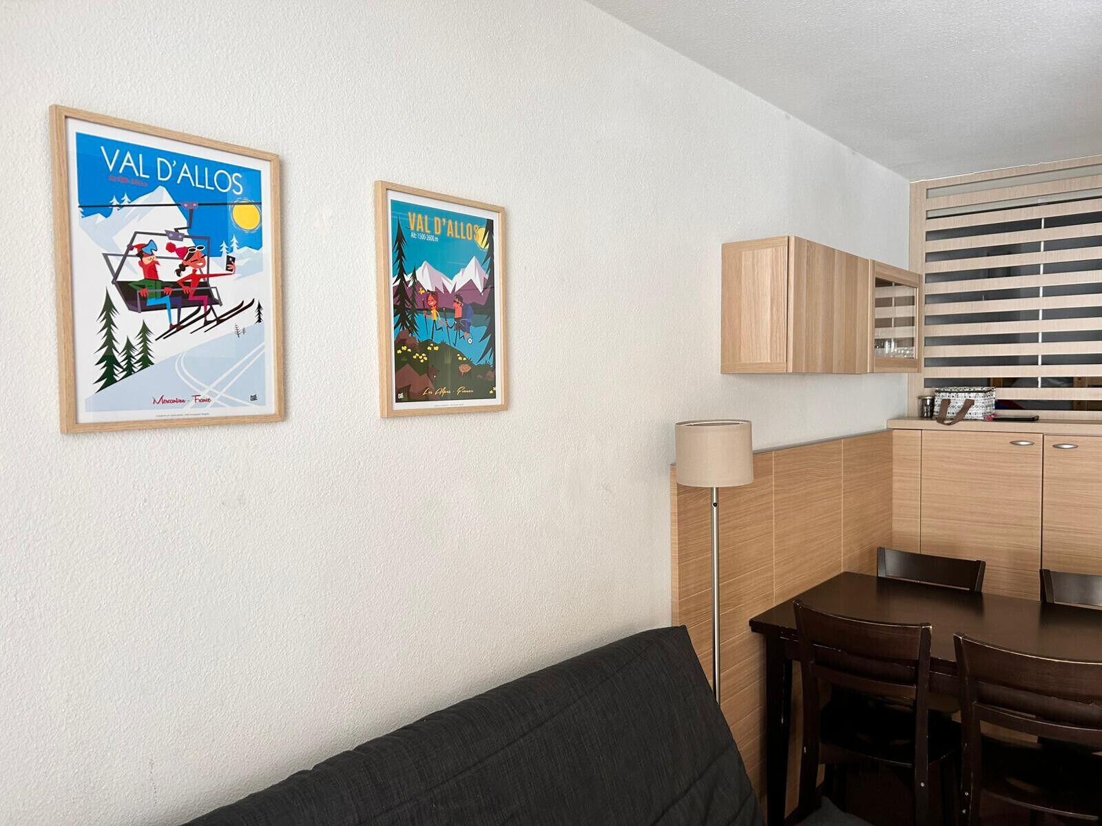 A modern room with a sofa, a dining table with chairs, a lamp, and two framed posters on the wall.