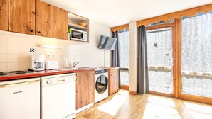 Een kleine keuken met houten kastjes, een magnetron, een koffiezetapparaat en een wasmachine.