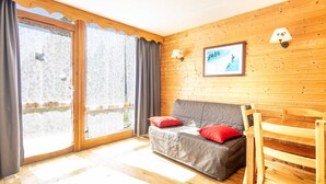 Een kamer met een houten wand, een grijze bank met rode kussens, een houten stoel en een lijst met een afbeelding aan de muur.