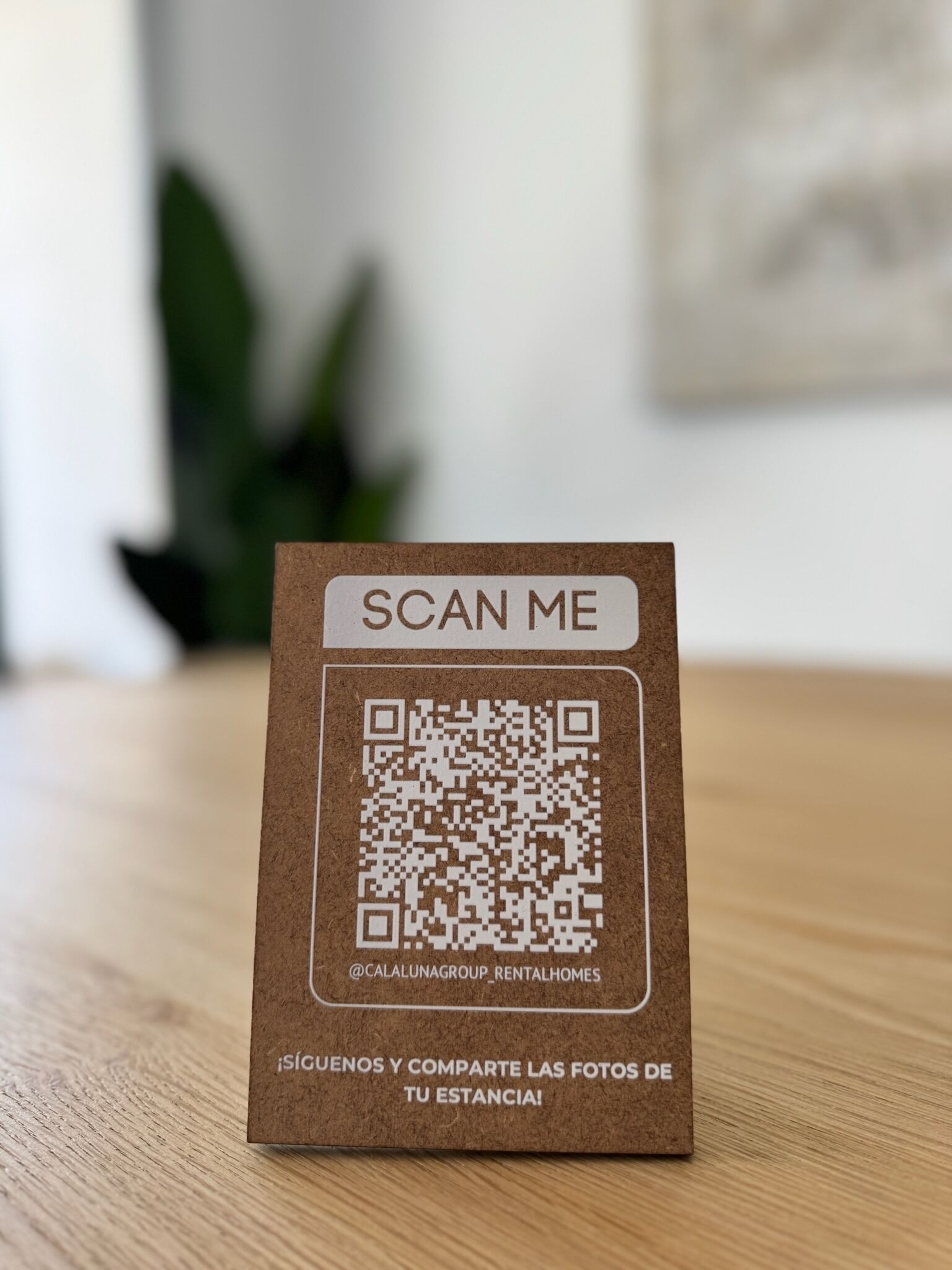 A QR code on a brown card with 'SCAN ME' at the top and a social media handle at the bottom.