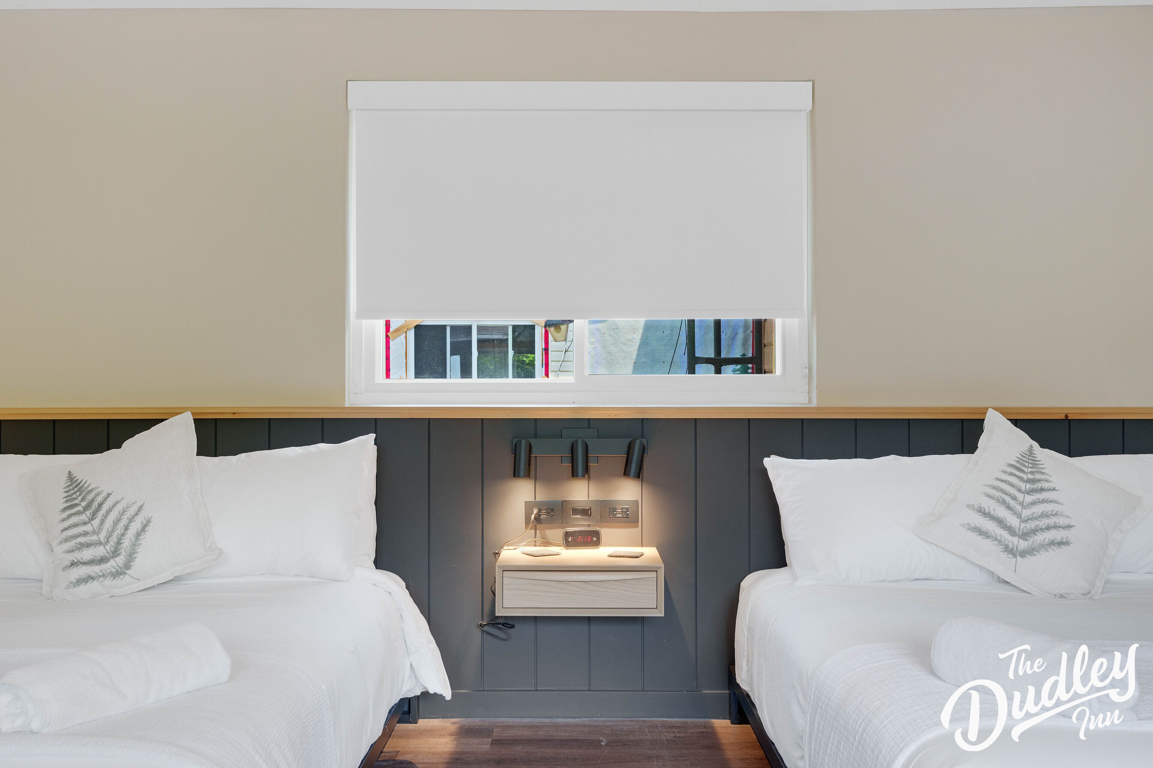A hotel room with two beds, a bedside table with a lamp, and a mounted artwork above the beds.