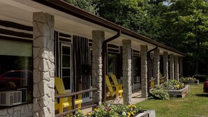 A covered outdoor area with stone pillars, yellow Adirondack chairs, and flower beds. - The Dudley Inn (Muskoka Lakes)