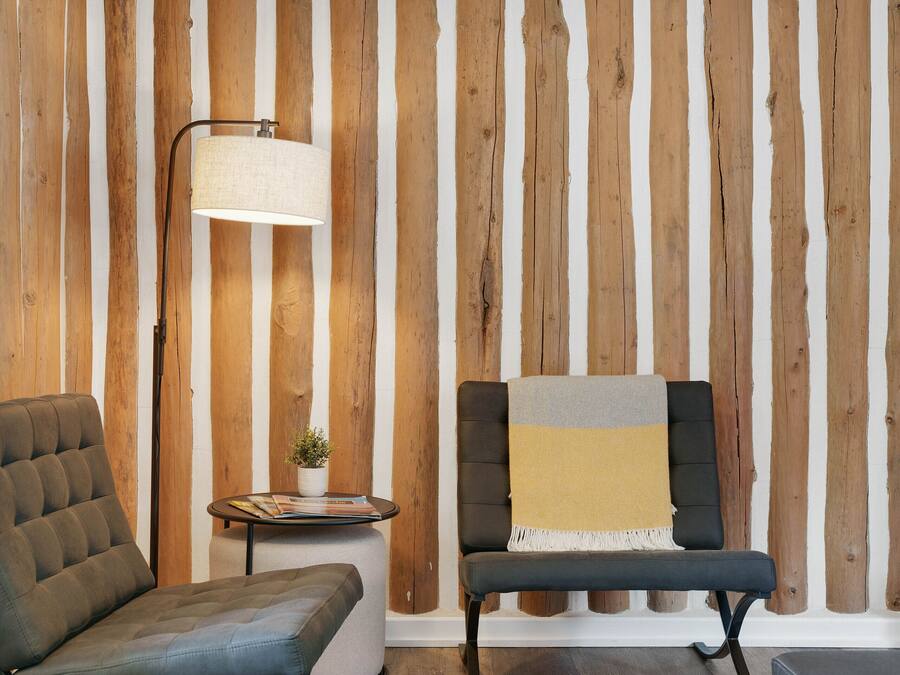 Et værelse med en væg af trælameller, en gulvlampe, en sofa, en bænk og et lille bord med en plante.