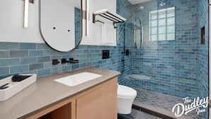 A modern bathroom with a large mirror, a sink, and a shower area. - The Dudley Inn (Muskoka Lakes)