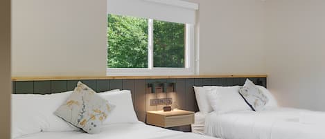 A hotel room with two beds, a nightstand with a clock, and a window with a view of greenery.