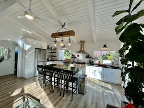A spacious kitchen with white cabinets, a central island with bar stools, and a hanging light fixture.