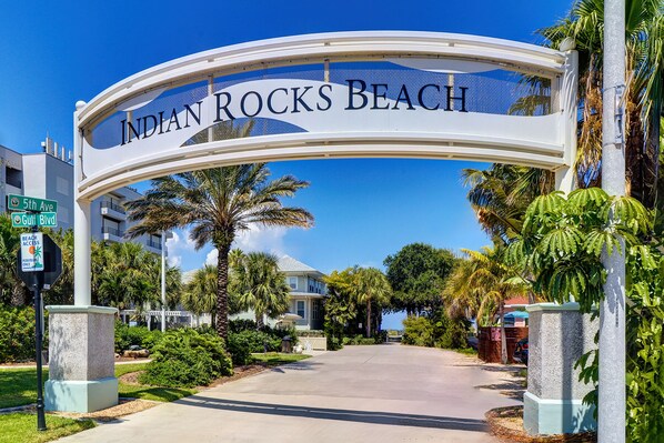 The entrance to Indian Rocks Beach with a clear sky, palm trees, and a sign indicating beach access.