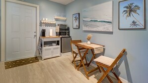 A compact kitchen with a microwave, toaster, and coffee maker, a dining area with a table and chairs, and a door with a decorative mat. - Private Surf Shack Less Than 5 Minutes to Indian Rocks Beach
Bikes Included! (Largo)