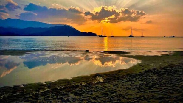 Un tramonto su un'acqua calma, con barche e montagne sullo sfondo.