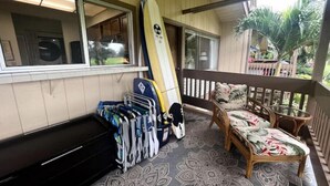 Un portico riparato con una tavola da surf appoggiata al muro, una panchina e una poltrona con cuscino floreale.