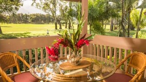 Un tavolo rotondo in vetro con sedie in vimini e un vaso di fiori rossi su un balcone che si affaccia su un campo da golf.