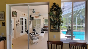 Un coin repas avec une table et des chaises en bois, une porte-fenêtre coulissante donnant sur un salon avec vue sur la piscine.