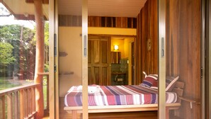 Une terrasse en bois avec un lit et un banc, une porte en bois, et une vue sur l’extérieur.