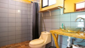 Une salle de bain comprenant des toilettes, un lavabo avec un récipient en verre et un rideau de douche.