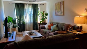 A living room with a brown leather sofa, a wooden coffee table, a lamp, and a painting on the wall. - Casa del Sol (Taos)