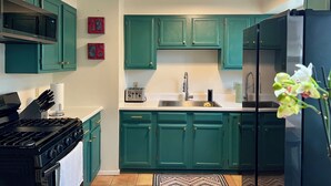 A kitchen with teal cabinets, a black stove, and a stainless steel refrigerator. - Casa del Sol (Taos)
