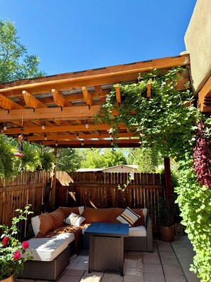 Un espace extérieur abrité, doté d’une pergola en bois, de sièges rembourrés et de plantes suspendues.