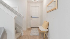 Un couloir avec une porte blanche, un banc avec un coussin, un miroir au mur et un escalier.