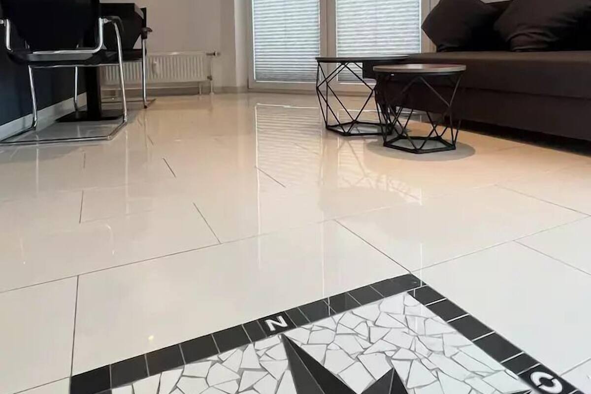 Ein modernes Wohnzimmer mit Fernseher, einer Couch, einem Couchtisch und einem großen Fenster mit Jalousien.