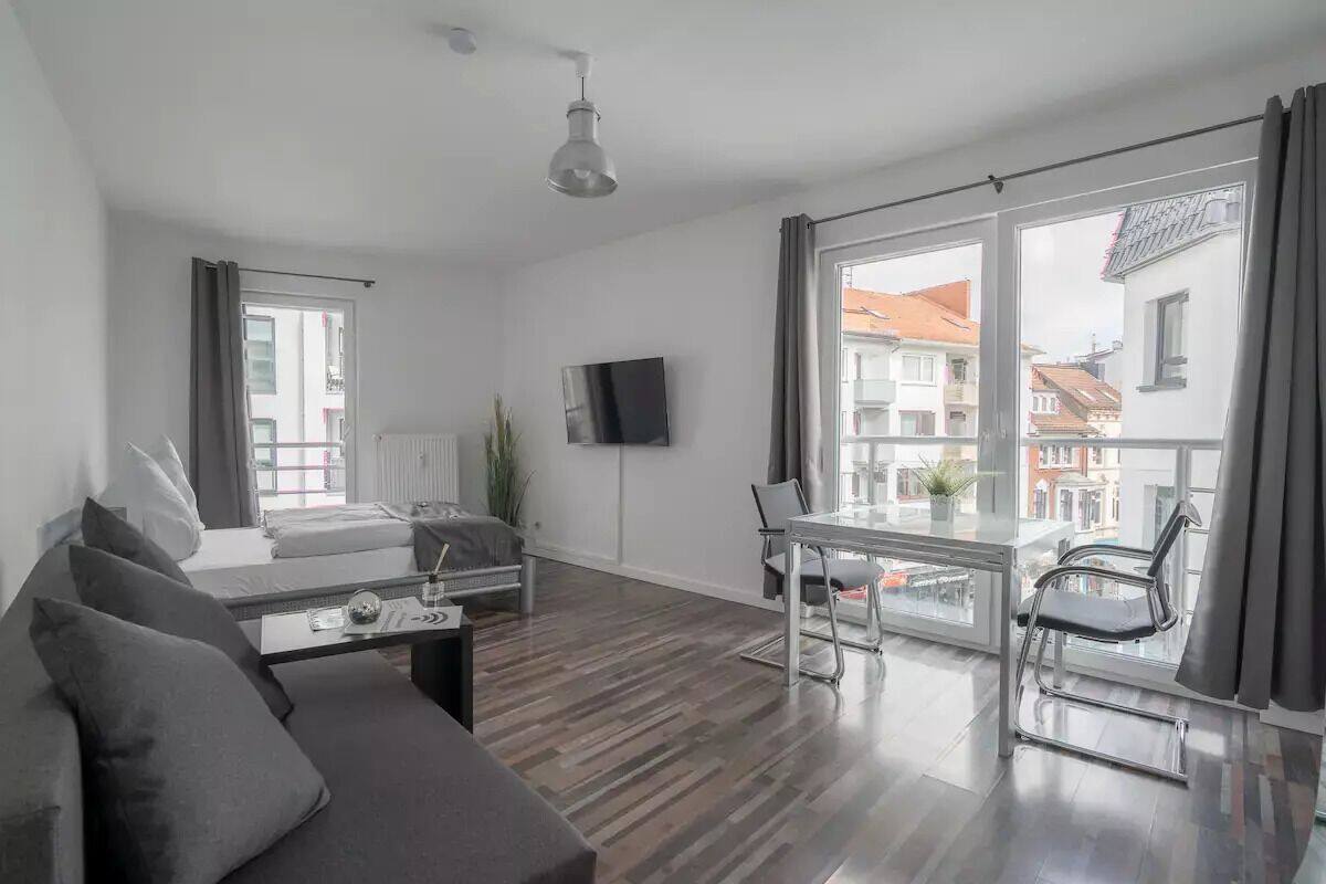 Ein modernes Wohnzimmer mit Sofa, Couchtisch, Wand-Fernseher und Balkon mit Tisch und Stühlen.