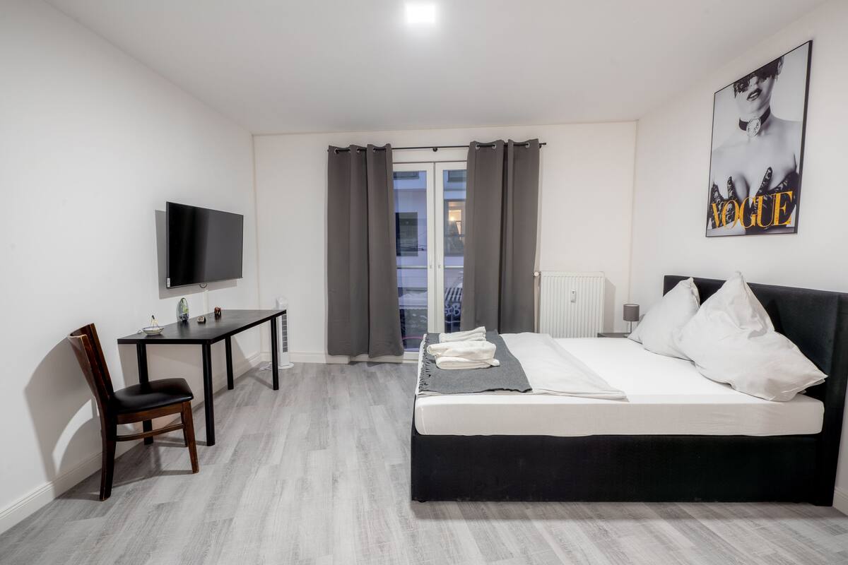 Ein modernes Hotelzimmer mit Bett, Schreibtisch, Stuhl, Fernseher und einem Fenster mit Vorhängen.