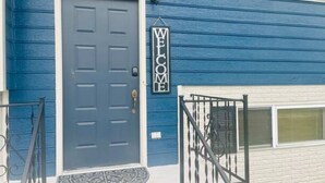 Una casa azul con puerta azul oscuro, un letrero de bienvenida y un pequeño porche con barandilla de metal.