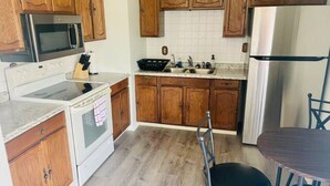 Una cocina con armarios de madera, un refrigerador de acero inoxidable, un microondas, una estufa, un fregadero y un taburete de bar.