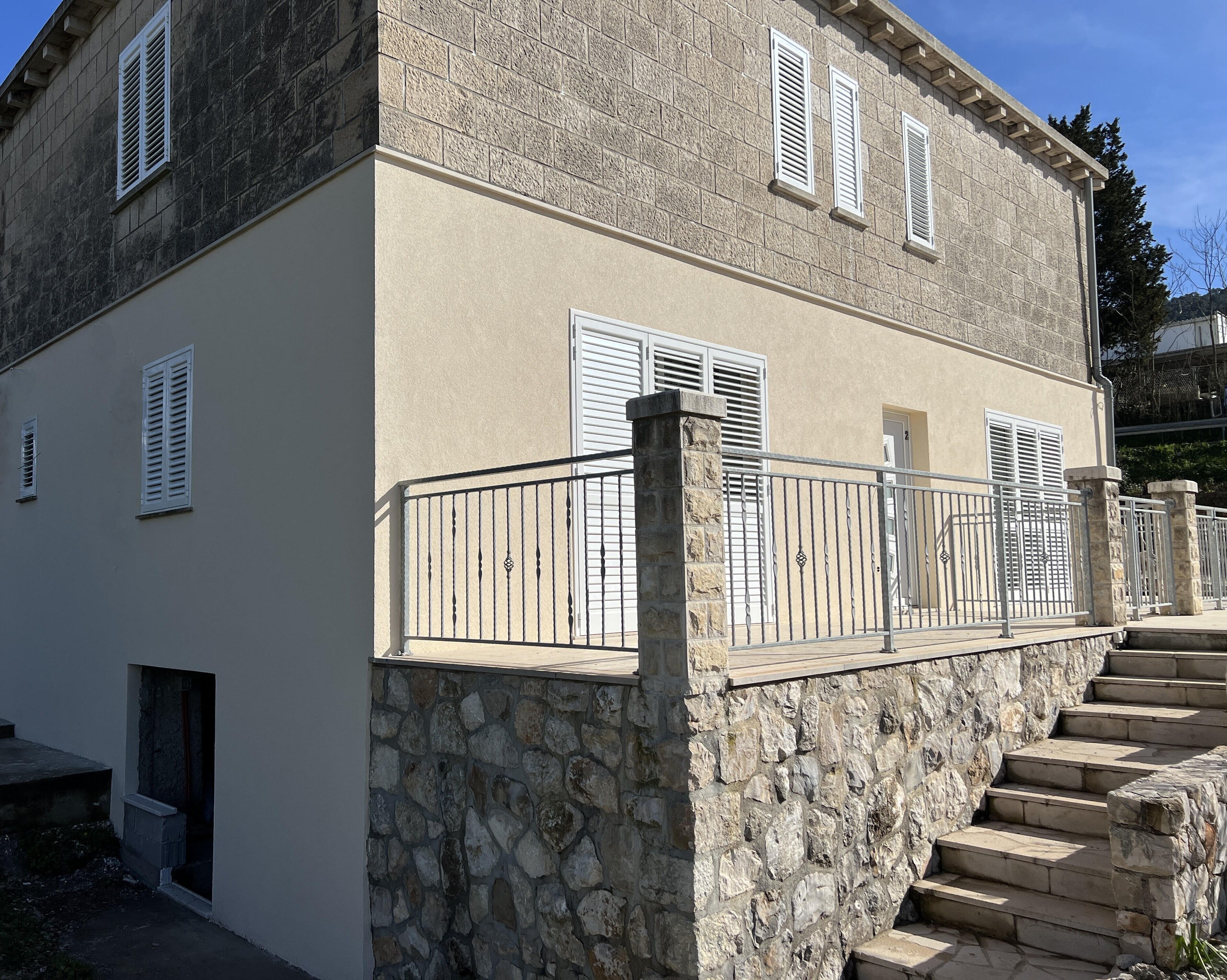 Un bâtiment à deux étages, doté de murs en pierre et de volets blancs, avec un escalier en pierre menant à l’étage supérieur.