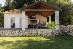 Outdoor kitchen with grill, table, and chairs, set amidst a tropical ambiance.