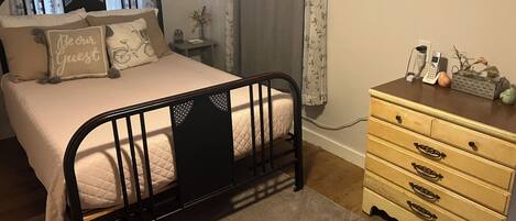 Ein Schlafzimmer mit Bett, Kommode, Nachttisch und einem Fenster mit Vorhängen.