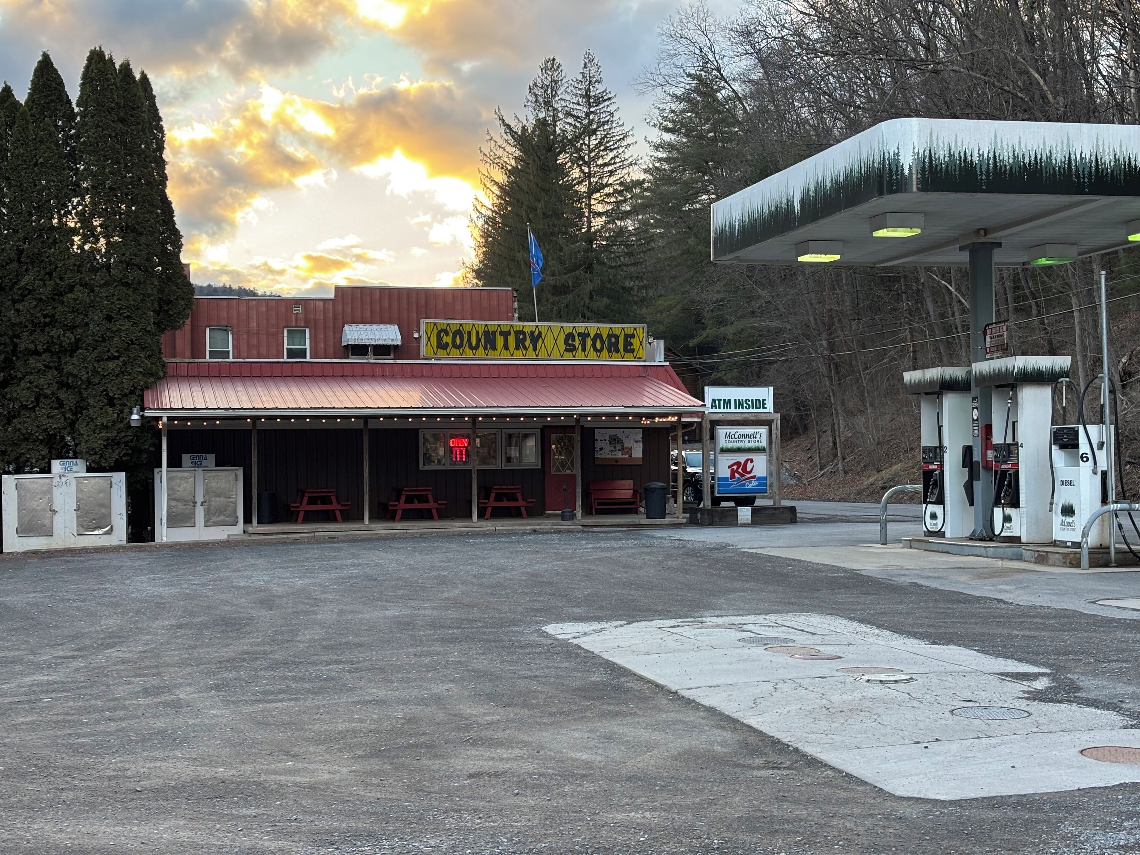 A country store with a red roof, outdoor seating, and a gas station with multiple pumps.
