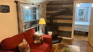 A cozy living room with a red sofa, a small table with a plant, a fireplace, and a window with curtains. - Cabin in Waterville- conv location, close to rail trail and Big Pine Creek (Waterville)