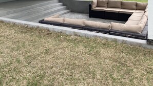 Eine überdachte Terrasse mit einer Eckcouch, einem Deckenventilator und einem an der Wand befestigten Fernseher.