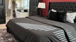 Ein Schlafzimmer mit einem großen Bett, einer roten Akzentwand, einem schwarzen Kopfteil und einem gemusterten Teppich.