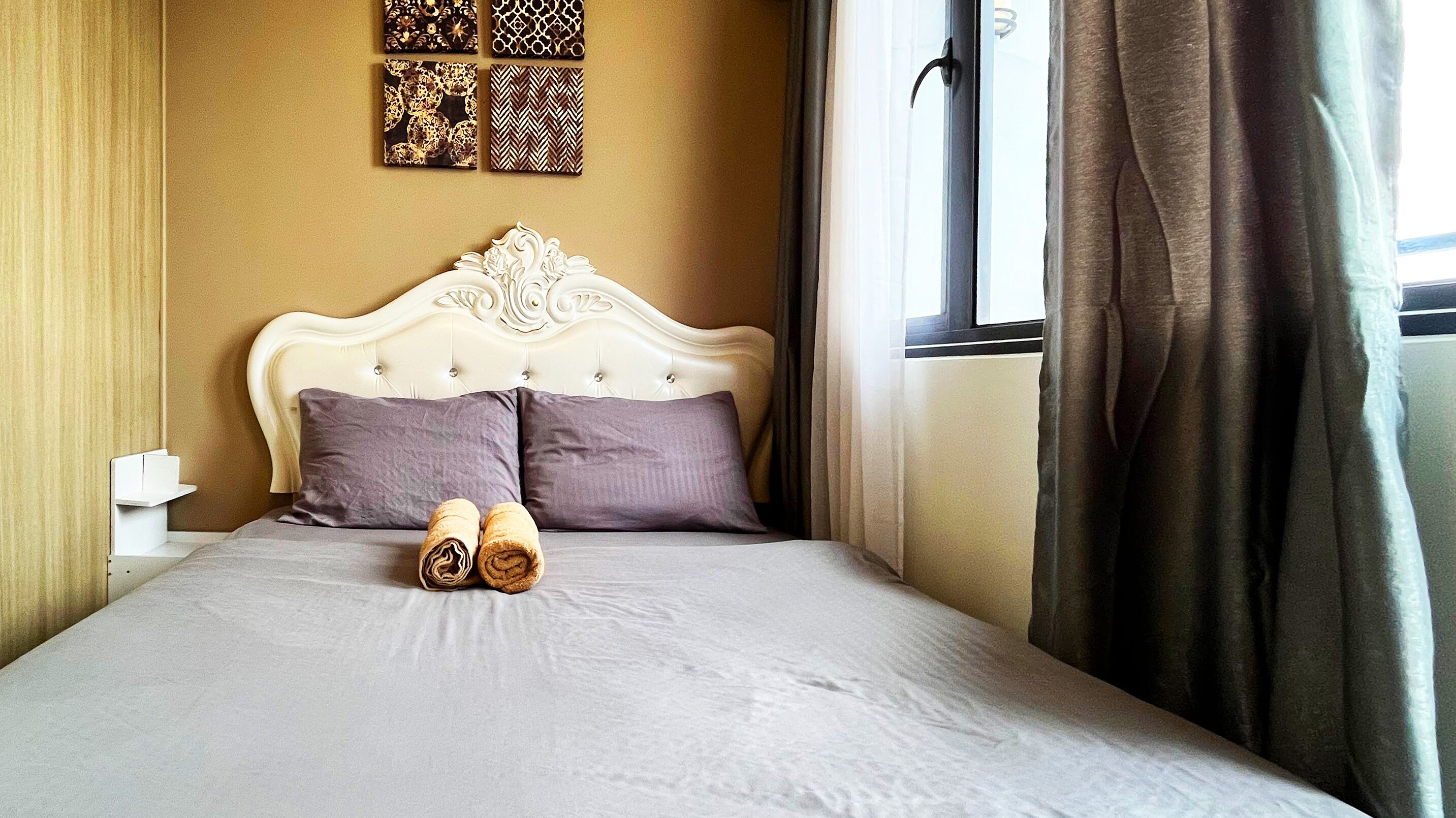 A neatly made bed with two pillows, a headboard, and two rolled towels on the bed.